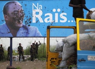 Presidential guardsmen stand under the stained campaign poster of Congolese President Joseph Kabila following clashes with supporters of opposition presidential candidate Etienne Tshisekedi at Kinshasa Airport.